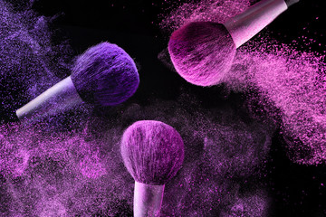 Three brushes for makeup with pink and purple make-up shadows in motion on a black background.