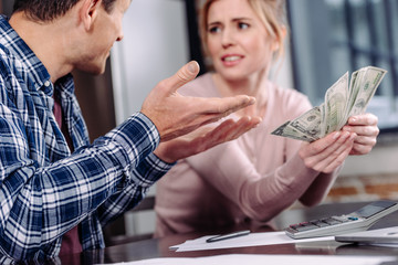 selective focus of couple with money sitting at table at home, financial problems concept