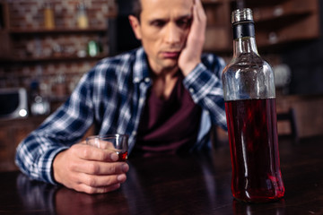 selective focus of depressed man sitting at table with bottle and glass of alcohol at home