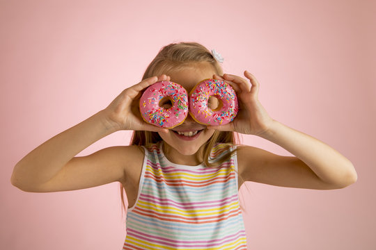 young beautiful happy and excited blond girl 8 or 9 years old holding two donuts on her eyes looking through them playing cheerful