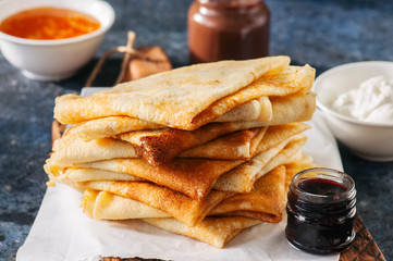 Delicious crepes (blinis) with assorted sauces on a wooden board on a blue stone background.