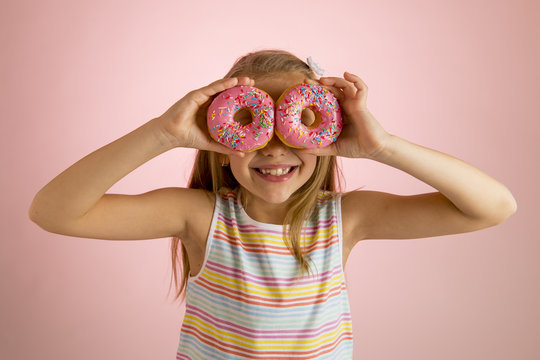 young beautiful happy and excited blond girl 8 or 9 years old holding two donuts on her eyes looking through them playing cheerful