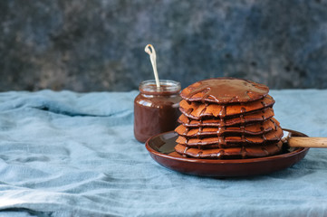 Chocolate pancakes wiyh syrup in a plate on a blue background.