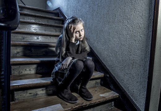 7 or 8 years old sad depressed and worried schoolgirl sitting on staircase desperate and scared suffering bullying and harassment at school