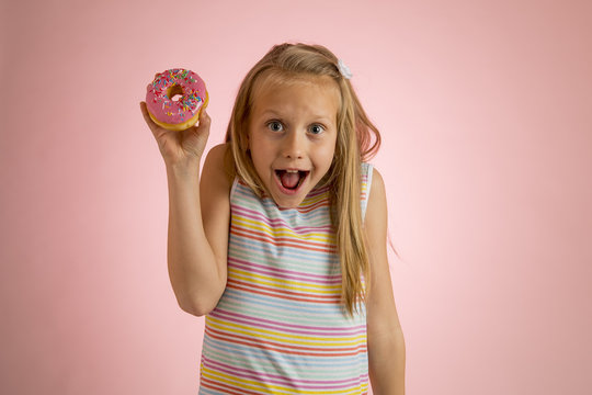 young beautiful happy and excited blond girl 8 or 9 years old holding donut desert on her hand looking spastic and cheerful in sugar abuse and addiction
