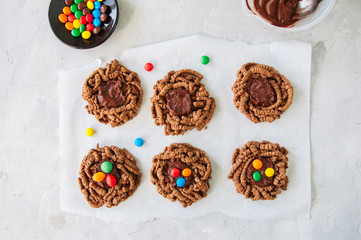 Chocolate bird's nest cookies decorated with colorful candies on a white background. Top view.