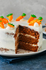 Carrot cake with cream cheese frosting decorated with carrot marmalade serving on a plate on a blue stone background.