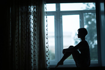 Fototapeta na wymiar Silhouette of sad girl sitting on window