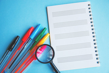 Colored pens and magnifier on a white sheet of notepad for text. Education or business concept