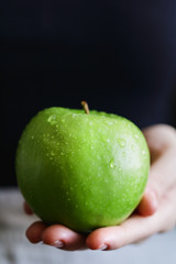 Girl is holding the fresh green apple in a hand. The concept of organic food and harvest.