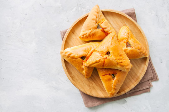 Homemade baked uchpuchmak (samsa) with meat and potato on a wooden plate on a white stone background. Top view and copy space.