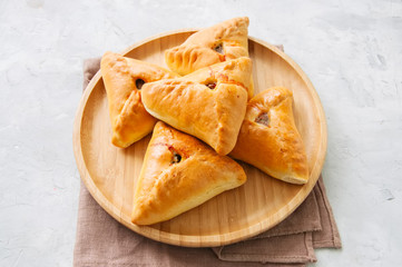 Homemade baked uchpuchmak (samsa) with meat and potato on a wooden plate on a white stone background. Overhead view and copy space.