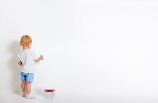 Little boy with paint brush and tin can standing back near white wall