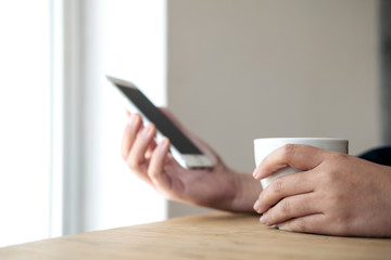 Closeup blur image of hands holding white mobile phone and coffee cup on wooden table