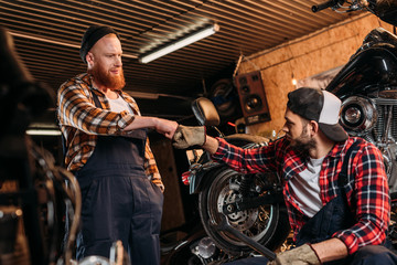 Fototapeta na wymiar handsome mechanics making bro fist at motorcycle repair garage
