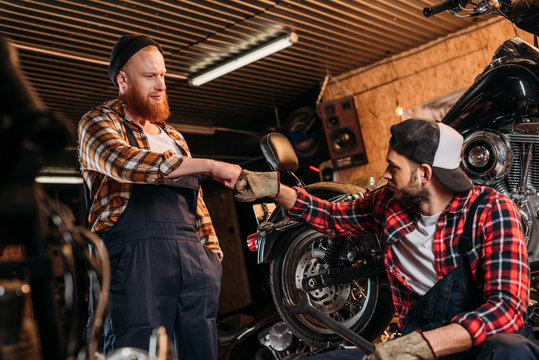 handsome mechanics making bro fist at motorcycle repair garage