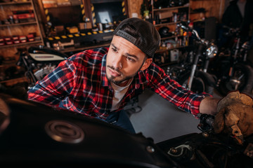 Plakat close-up shot of handsome bike repair station worker looking at motorcycle at garage