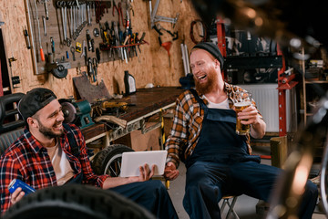 laughing mechanics with tablet and beer at garage