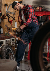 Obraz na płótnie Canvas handsome bike repair station worker using electric circular saw at garage