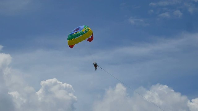 4K parasailing activity. colorful parasailing wing flying with tourist in the blue cloudy sky, extreme sport, summer activities at the beach