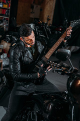 Fototapeta na wymiar handsome young man playing guitar while sitting on bike at garage