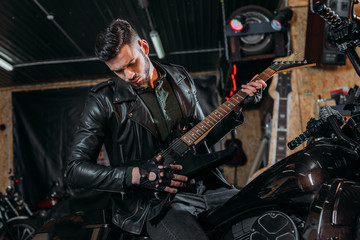 Fototapeta na wymiar handsome young man playing guitar while sitting on bike at garage