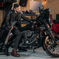 Fototapeta na wymiar stylish young man sitting on bike with electric guitar at garage