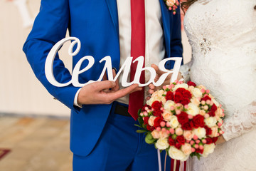 The bride in white dress and groom in blue suit holding wooden inscription “Family”. Wedding décor
