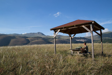 hiker sits at a picnic table with beautiful panorama, in the horizon the mountain village castel del monte and monte camicia