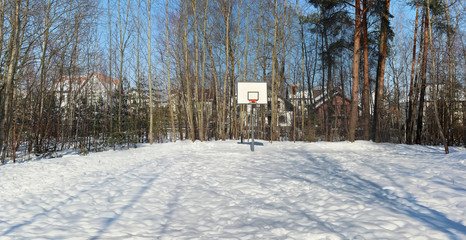 An empty basketball court in a snow-covered forest near a European village