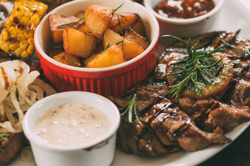 close-up view of roasted potatoes, grilled vegetables and meat with sauces on plate