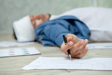 Business man Fainted On Floor In Office.Unconscious Young Businessman Lying with Graphs and charts work hard