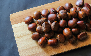 Fresh chestnuts on dark black rustic background. Pile of fresh chestnuts ready to roast shot over black antique background. Top view.