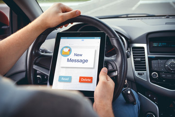 A young man with a tablet in his hand at the wheel of the car.