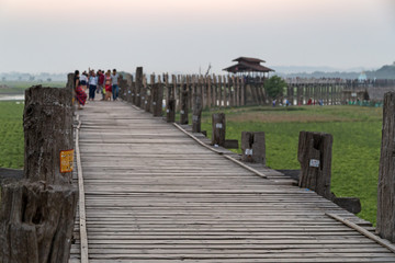 Obraz premium Some people at the U Bein Bridge at Amarapura near Mandalay in Myanmar (Burma) at dusk. It's the oldest and longest teakwood bridge in the world. Focus on the foreground.