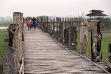 Fototapeta premium Few people at the U Bein Bridge at Amarapura near Mandalay in Myanmar (Burma) at dusk. It's the oldest and longest teakwood bridge in the world. Focus on the foreground.