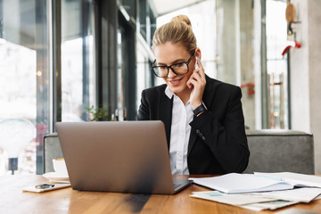Fototapeta premium Smiling blonde business woman sitting by the table in cafe