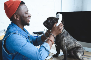 Handsome african american man wearing headphones on French bulldog on computer table