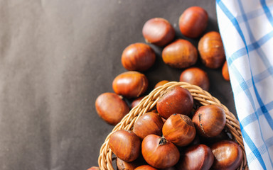 Fresh chestnuts on dark black rustic background. Pile of fresh chestnuts ready to roast shot over black antique background. Top view.
