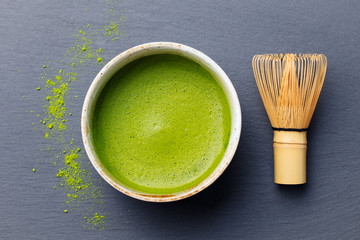 Matcha green tea cooking process in a bowl with bamboo whisk. Black slate background. Top view.