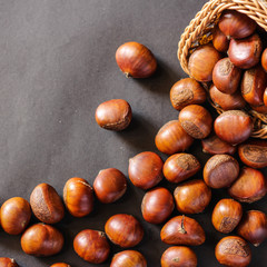 Fresh chestnuts on dark black rustic background. Pile of fresh chestnuts ready to roast shot over black antique background. Top view.