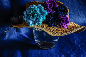 straw hat with artificial flowers in vintage style worn on glass vase