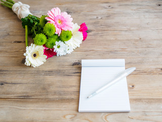  Notizblock,  Blumenstrauß und ein Kugelschreiber auf einem braunen Holztisch. Frühling, Büro, Lifestyle, Tagebuch.