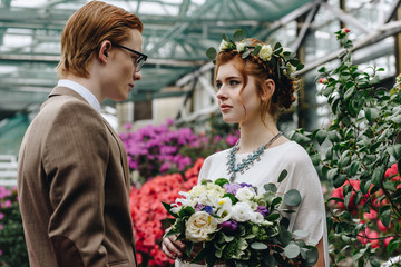 stylish young groom and beautiful redhead bride looking at each other in botanical garden