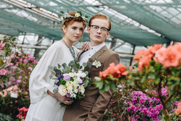 beautiful elegant young red-haired wedding couple standing together between flowers in botanical garden
