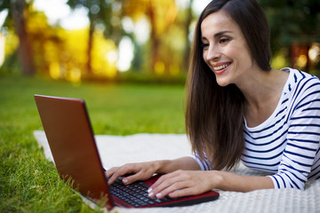 Amused brunette woman working with her notebook lying on a lawn in the park