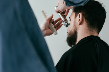 Fototapeta premium cropped image of barber trimming customer beard at barbershop