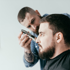 side view of barber trimming customer beard at barbershop isolated on white