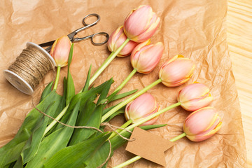 Tulipanes rosas junto a una tijera e hilo sisal sobre un fondo de papel marrón arrugado. Vista superior y de cerca.