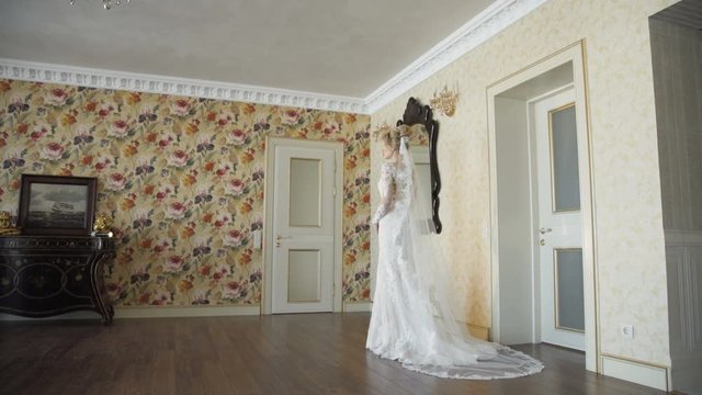 Back view of beautiful bride stands in wedding dress with vail in room